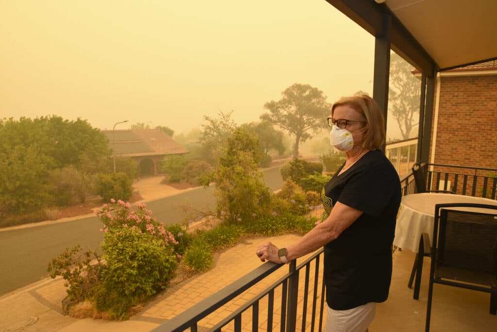 A woman, on a balcony, wears a face mask to protect herself against very dangerous level of air pollution. A thick yellow fog coming from the nearby forest fires.